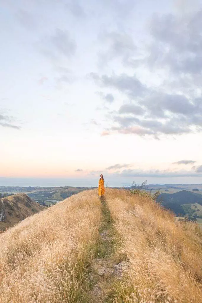 wide shot of girl wrapped in throw overlooking new zealand landscape